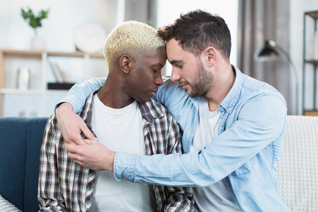 Multi ethnic same sex couple embracing together on couch